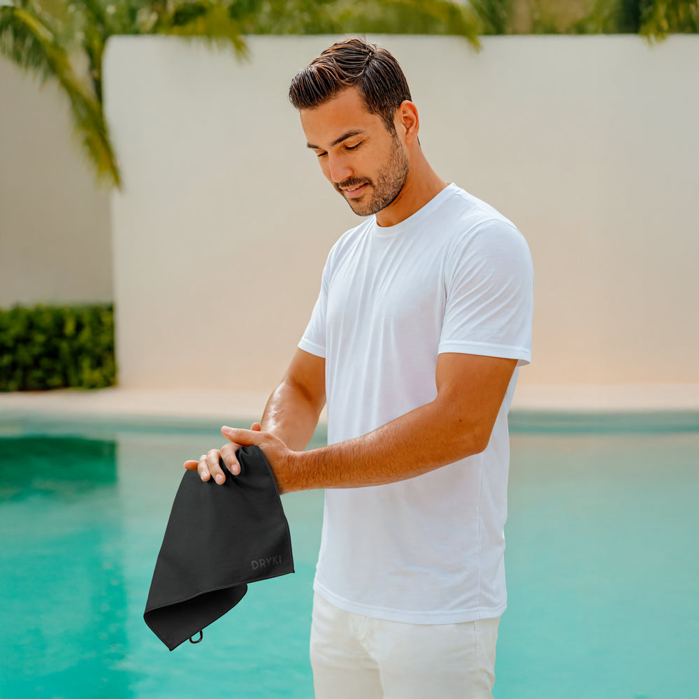 Man holding a black towel by a pool, wiping hands with a DRYKI Pocket-sized sweat towel (sweat absorbing handkerchief)